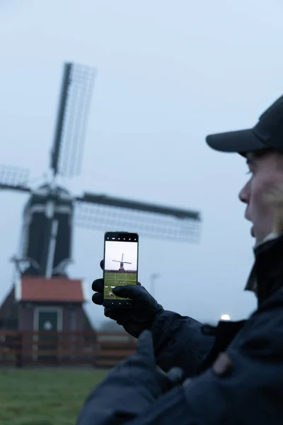 Sabahın köründe telefonuyla yel değirmeninin fotoğrafını çeken adam.