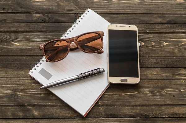 Cep telefonu, defter, kalem ve gözlüklü ahşap bir masa görüntüsü
