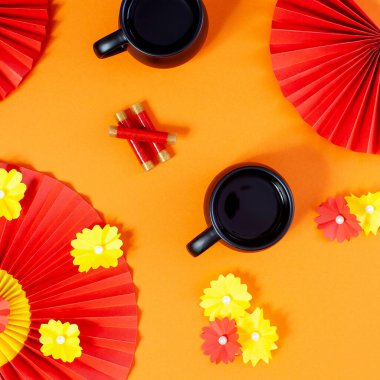 Çay fincanlarıyla Çin Yeni Yılı kompozisyonu, çiçekli kırmızı kağıt fanlar ve pastel turuncu arka planda kestane fişekleri..