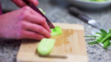Person cutting vegetables on a wooden kitchen board (cucumber sliced)