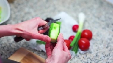 Person cutting vegetables in a kitchen (cucumber) - Salad with tomatoes, cucumbers, vegetables and green onions