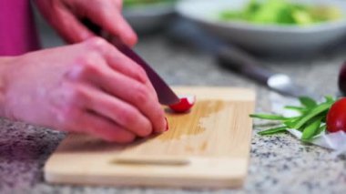 Person cutting vegetables on a wooden kitchen board (radish sliced)