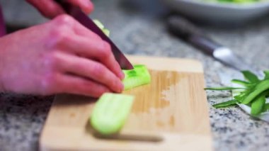 Person cutting vegetables on a wooden kitchen board (cucumber sliced)