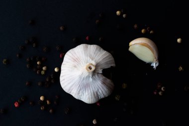 Close-up macro shot of a garlic in a dark background surrounded by peppercorns
