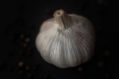 Close-up macro shot of a garlic in a dark background surrounded by peppercorns