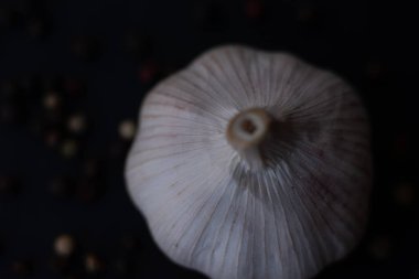 Close-up macro shot of a garlic in a dark background surrounded by peppercorns