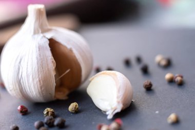 Close-up macro shot of a garlic in a dark background surrounded by peppercorns