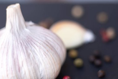Close-up macro shot of a garlic in a dark background surrounded by peppercorns