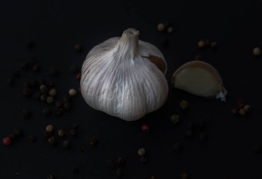Close-up macro shot of a garlic in a dark background surrounded by peppercorns
