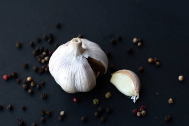 Close-up macro shot of a garlic in a dark background surrounded by peppercorns
