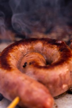 Close up shot of rolled up sausages on skewer placed over barbeque
