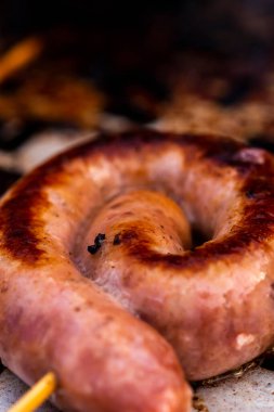Close up shot of rolled up sausages on skewer placed over barbeque