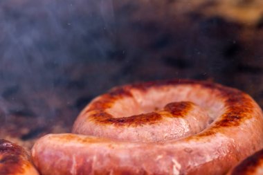 Close up shot of rolled up sausages on skewer placed over barbeque