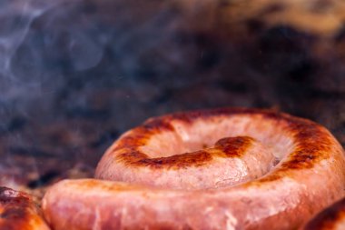 Close up shot of rolled up sausages on skewer placed over barbeque