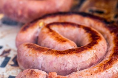 Close up shot of rolled up sausages on skewer placed over barbeque