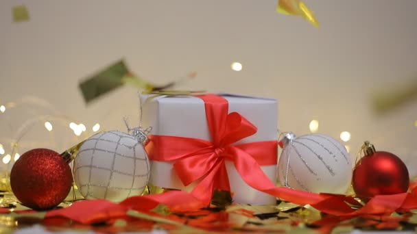 Χριστουγεννιάτικη σύνθεση. Χρυσά κομφετί πέφτουν σε κουτί δώρου και Χριστουγεννιάτικες μπάλες — Αρχείο Βίντεο