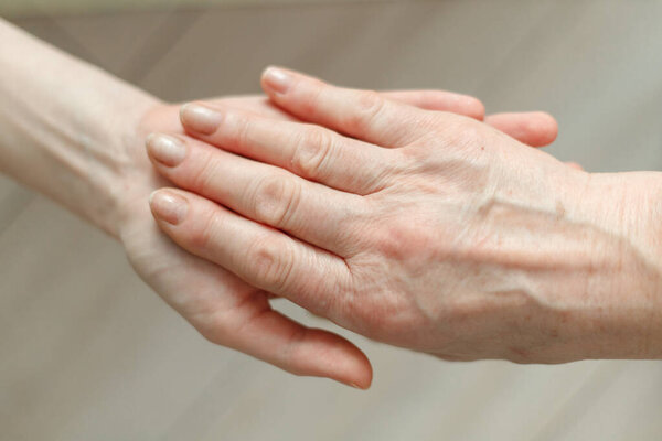 Hand of young girl holds hand of elderly mother. Older generation support