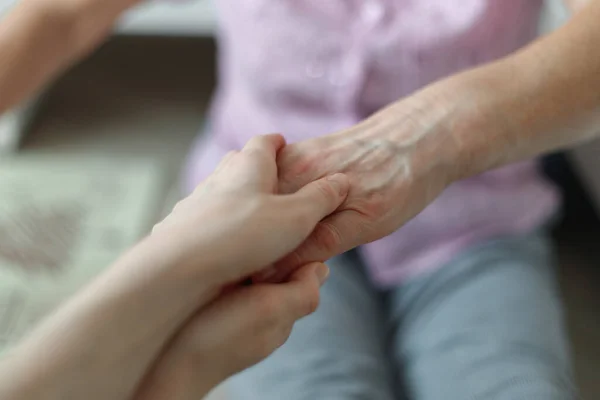 En ung flickas hand håller hand med en äldre mor. Äldre generationens stöd. — Stockfoto