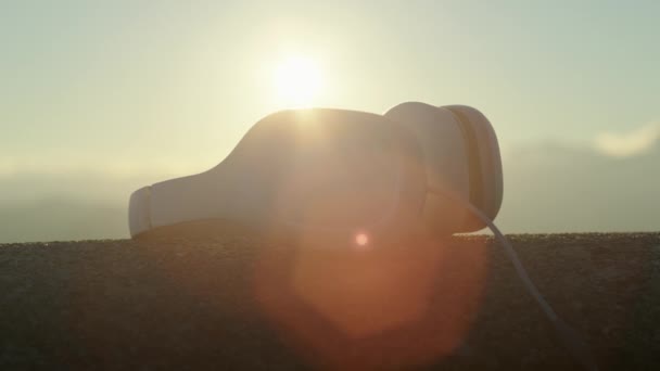 Håller hörlurar i luften vid solnedgången ljus — Stockvideo