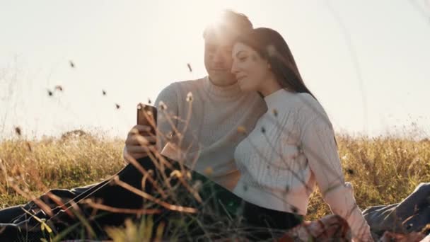 Αρραβωνιασμένο ζευγάρι κοιτάζει το κινητό τηλέφωνο στο φως του ήλιου — Αρχείο Βίντεο