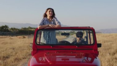 Kolları açık, kırmızı jipli bir kız yoldan çıkıyor. 