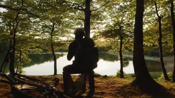 Αγόρι με σακίδιο κάθεται κοντά στη λίμνη το ηλιοβασίλεμα — Αρχείο Βίντεο