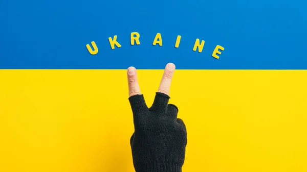Ruka s symbolem vítězství na pozadí ukrajinské vlajky — Stock fotografie
