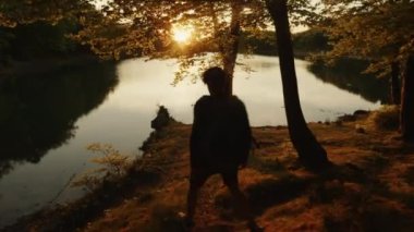 Sırt çantalı çocuk dağlarda göl kenarında yürüyor.