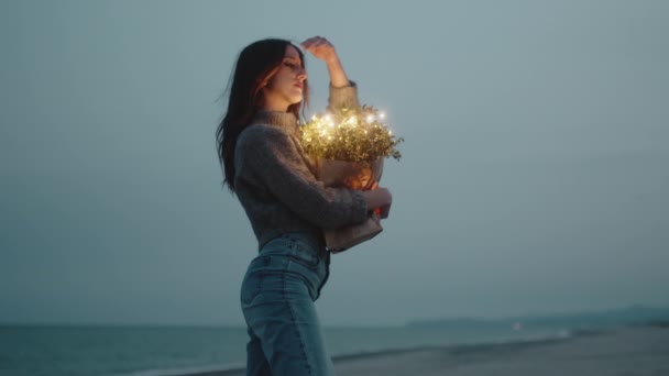 Glückliches junges Mädchen genießt das Leben am Strand mit bunten Lichtern auf der Tasche — Stockvideo