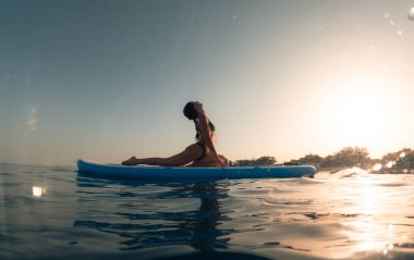 Bikinili kadın kürek çekme tahtasında vücut ağırlığı egzersizi yapıyor.
