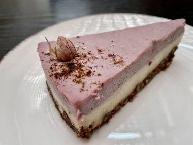 Siyah ahşap bir masada duran beyaz tabakta duran lezzetli bir ahududulu çiğ peynirli kek. Yüksek kalite fotoğraf