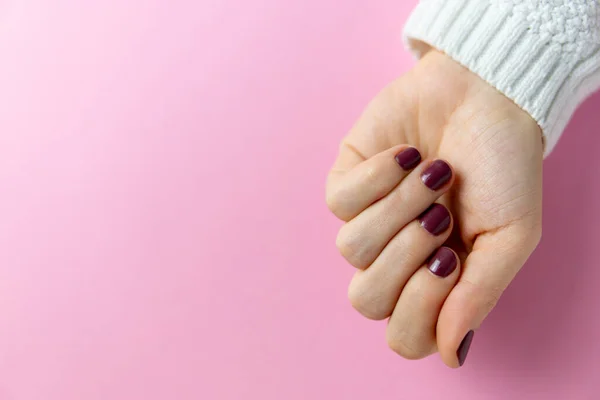 Closed hand on pink background with freshly done and painted nails