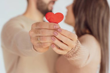 Small red heart held by the hands of an unrecognizable couple as they embrace and gaze at each other.