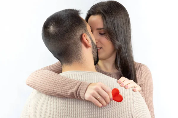 Couple in love embracing while looking at each other and she holding a red heart in her hand on a white background.