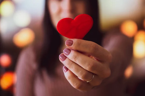 Unrecognizable young girl holding a small red heart in the foreground