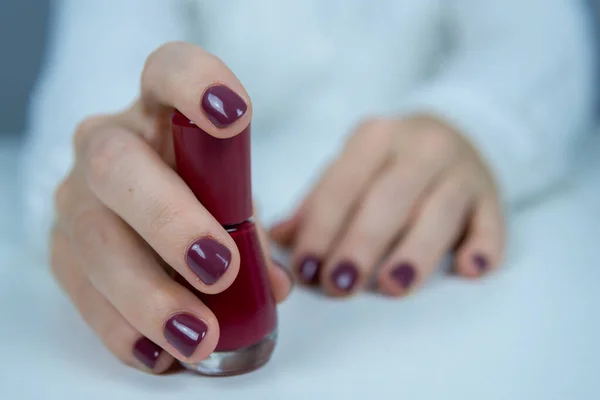 Elinde cam bir oje şişesi ve manikürlü tırnakları olan genç bir kızın eli..