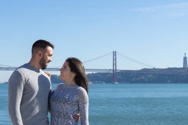 Birbirine bakan bir çift ve arka planda 25 Nisan köprüsü, Lizbon, Portekiz.