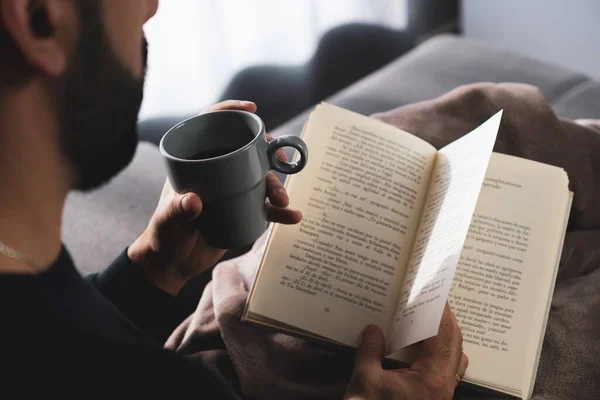 Tanımlanamayan bir adam evinde, kanepede oturmuş kahve içerken kitap okuyor..