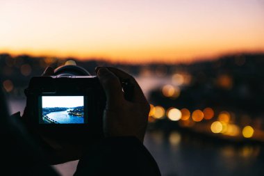 Tanımlanamayan fotoğrafçı, elinde kamerayla Douro nehrinin ve Porto şehrinin günbatımında fotoğraflarını çekiyor..