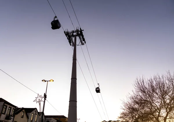 Alacakaranlıkta porto teleferiği, güneş tarafından aydınlatılmış bir ağaç ve Noel zamanı lamba direklerindeki ışıklar..