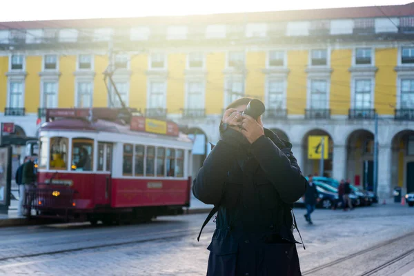 Lizbon, Portekiz 11-27-2021, Lizbon ticaret meydanında fotoğraf çeken genç fotoğrafçı, ve kırmızı bir turist tramvayı arkasında..