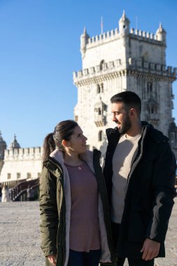 Güneşli bir kış gününde Belem Kulesi 'nin yanındaki Tagus Nehri kıyısında birbirlerine bakan çift..