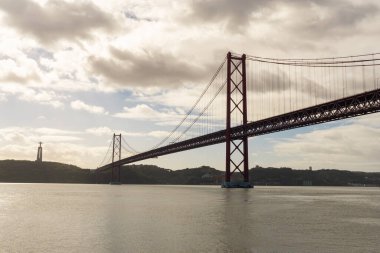 25 Nisan köprüsü, bulutlu bir sonbahar gününde, Tagus nehrinin üzerinde ve arka planda Kral İsa 'nın heykeli.