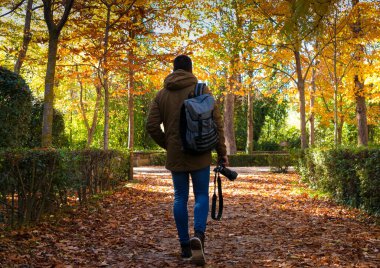 Bir sonbahar gününde elinde kamerayla parkta gezinen bir adam.