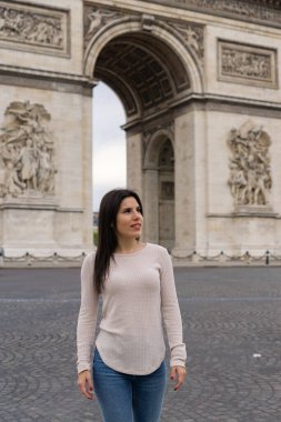 Paris 'te Zafer Kemeri' nin arkasında poz verirken gülümseyen ve mutlu genç bir kadın turist.