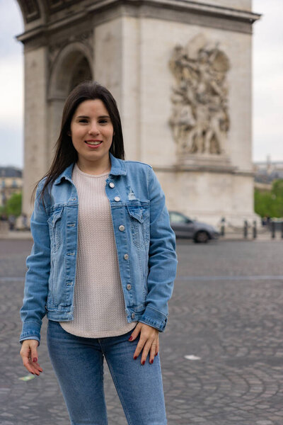 Close-up of a young woman tourist smiling and happy while posing and behind the Triumphal Arch in paris.