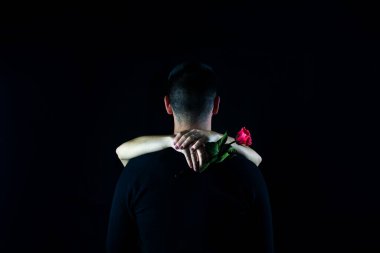 Unrecognizable boy on his back embraced by his wife with a rose in his hand with black background