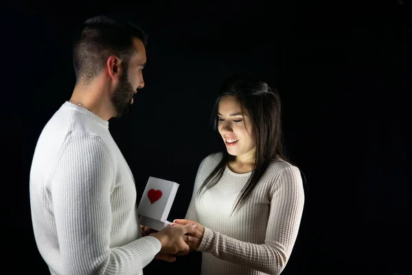 Man giving a gift to his wife on valentine's day with a black background.