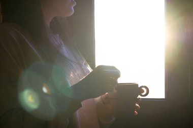 Tanımlanamayan genç bir kadın bir fincan kahveden zevk alıyor pencereden dışarı bakıyor.