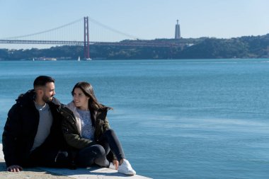 Arka planda 25 Nisan köprüsü olan genç çift, Lizbon, Portekiz